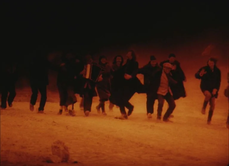 Russian Symphony (1994) movie still: wide — A group of people move across a dark, dusty, and barren landscape at night. One individual plays an…