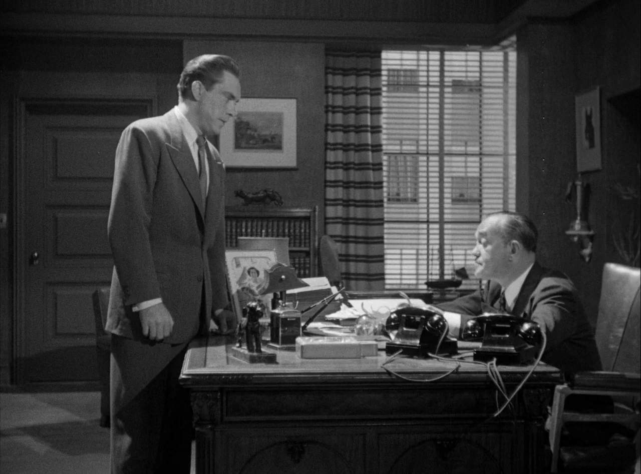 The Killers (1946) movie still: medium — A 1940s professional wood-paneled room contains a large desk and window blinds. A man in a suit stands…