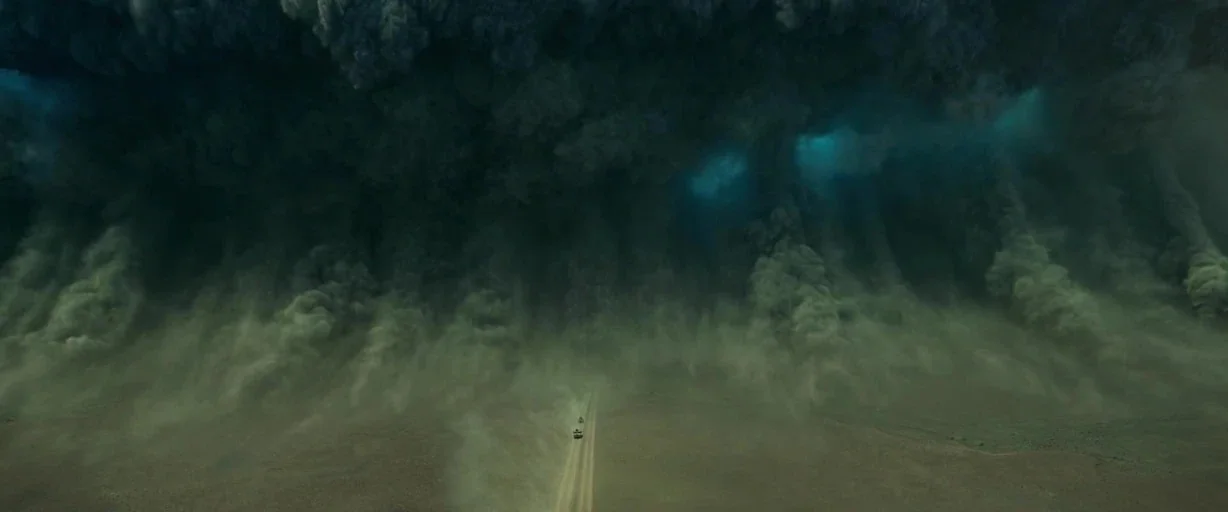 Monster Hunter (2020) movie still: establishing — A gargantuan wall of dark storm clouds and swirling dust looms over a desert. Two small vehicles…