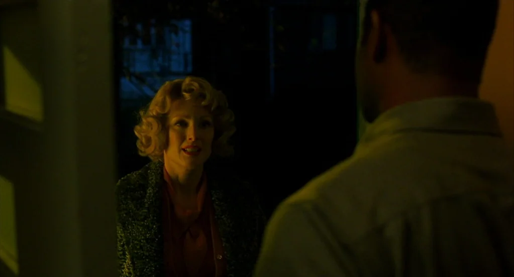 Far From Heaven (2002) movie still: medium — An interior doorway at night frames a woman illuminated by soft interior light. She stands facing a man…