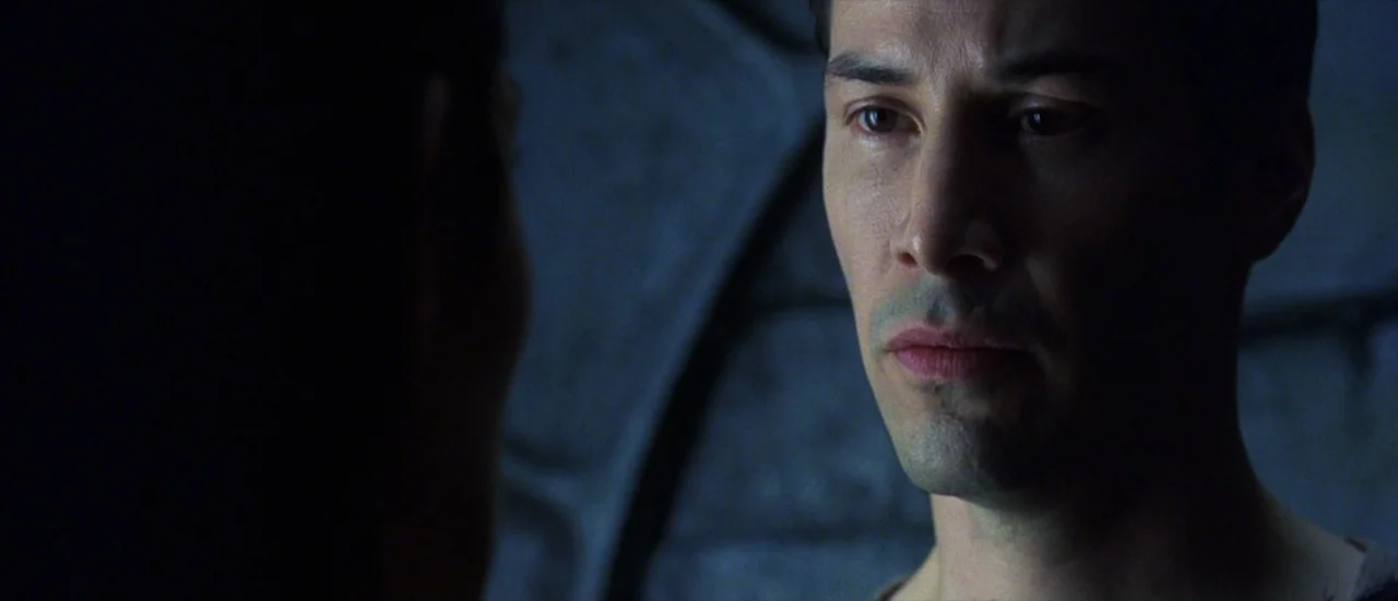 The Matrix Revolutions (2003) movie still: closeup — A dark, metallic-walled interior room features shadows across a curved structure in the…