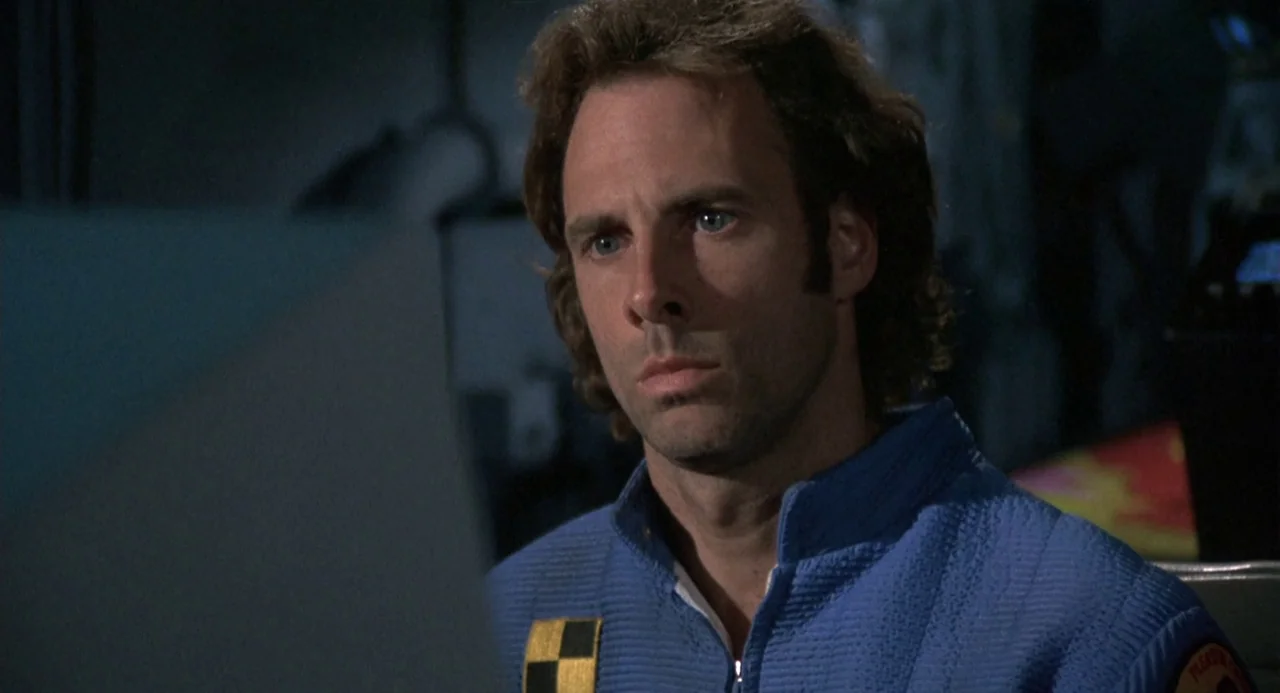 Silent Running (1972) movie still: closeup — A man in a blue flight suit sits in a dimly lit enclosure. He stares fixedly at an unseen display or…