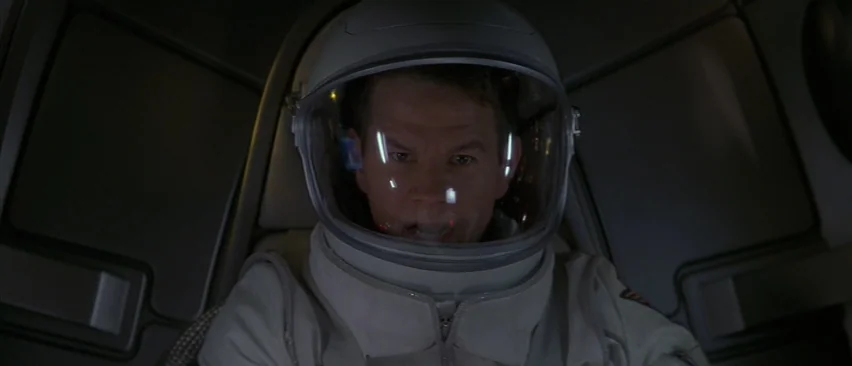 Planet of the Apes (2001) movie still: closeup — A dimly lit interior of a spacecraft cockpit features a pilot in a flight suit. The man gazes…