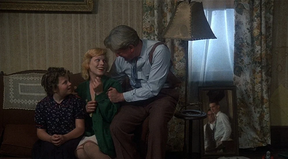 Thieves Like Us (1974) movie still: medium — A 1940s living room features floral patterned wallpaper and a window with lace curtains. A man in a…
