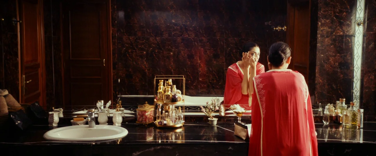 Animalia (2023) movie still: medium — A luxury bathroom features dark marble wall tiles and a polished black stone countertop. A woman in a red robe…