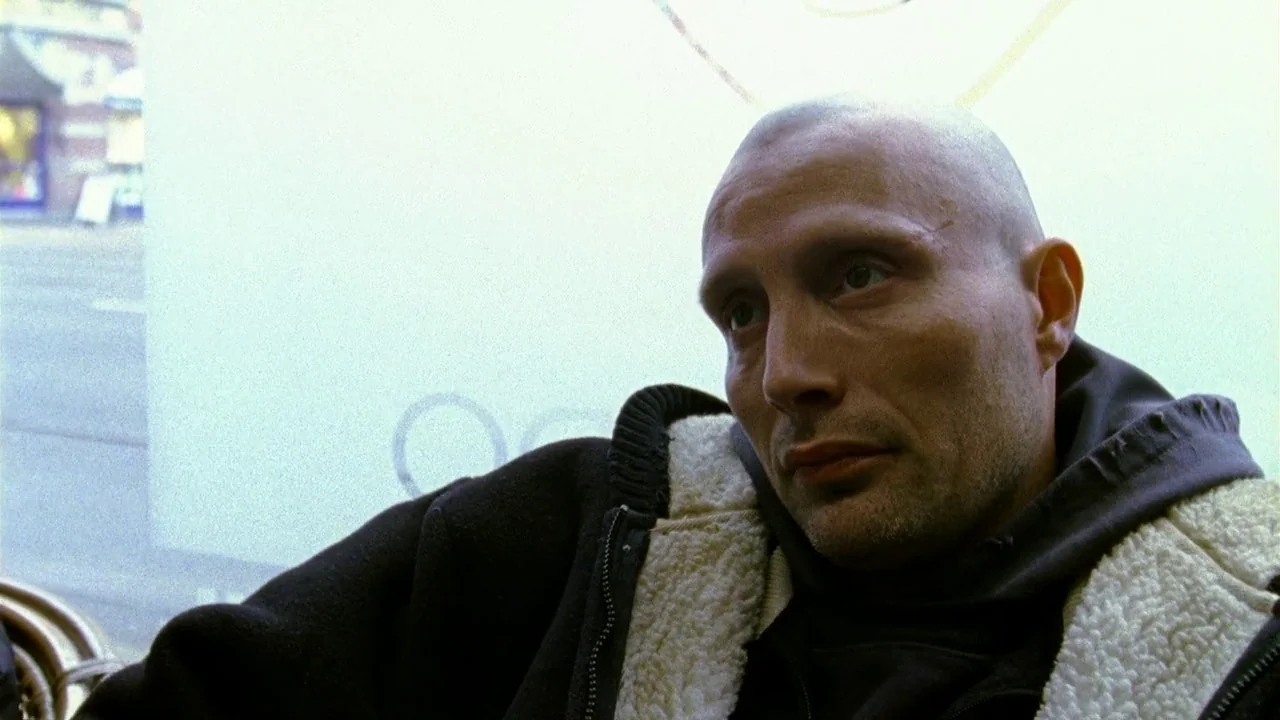 Pusher II (2004) movie still: closeup — A man sits before a bright window inside a public establishment during the day. He faces off-screen while…