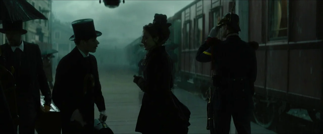 Tchaikovsky’s Wife (2022) movie still: wide — A rain-dampened 19th-century railway platform features a long, dark red vintage passenger train…