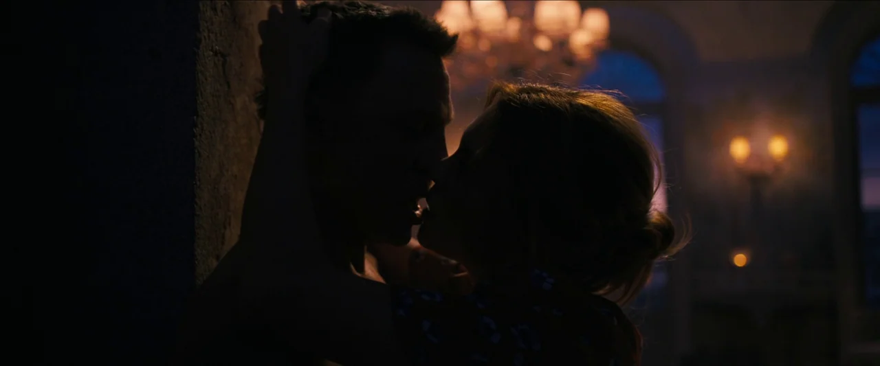 No Time To Die (2021) movie still: medium — A dark, elegant room with arched windows and glowing warm chandeliers in the background. A man and a…