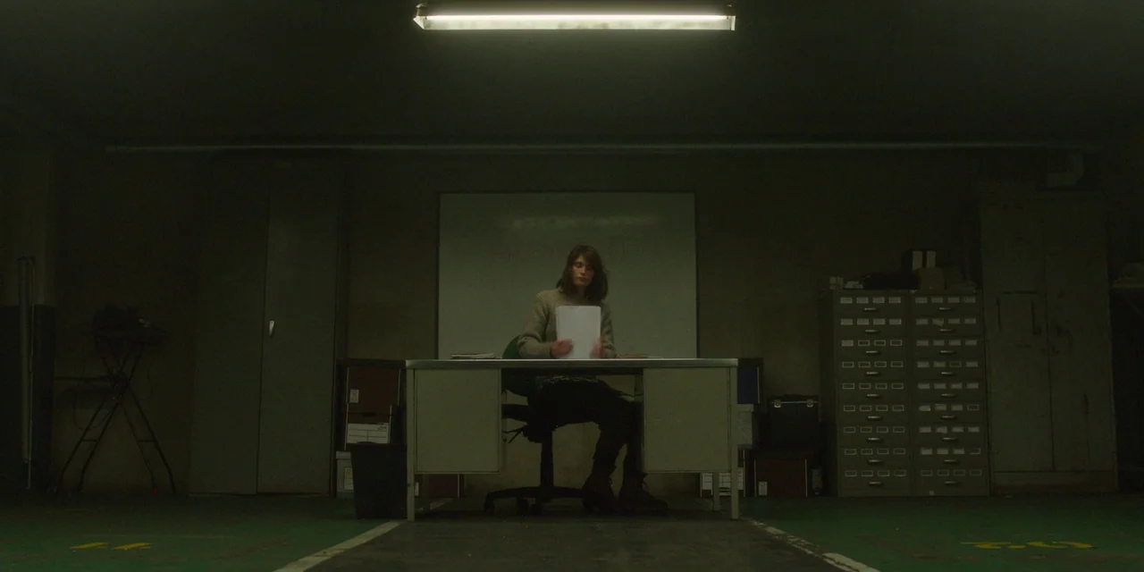 The Girl With All The Gifts (2016) movie still: wide — A dimly lit storage basement features a metal desk positioned in front of a whiteboard. A…