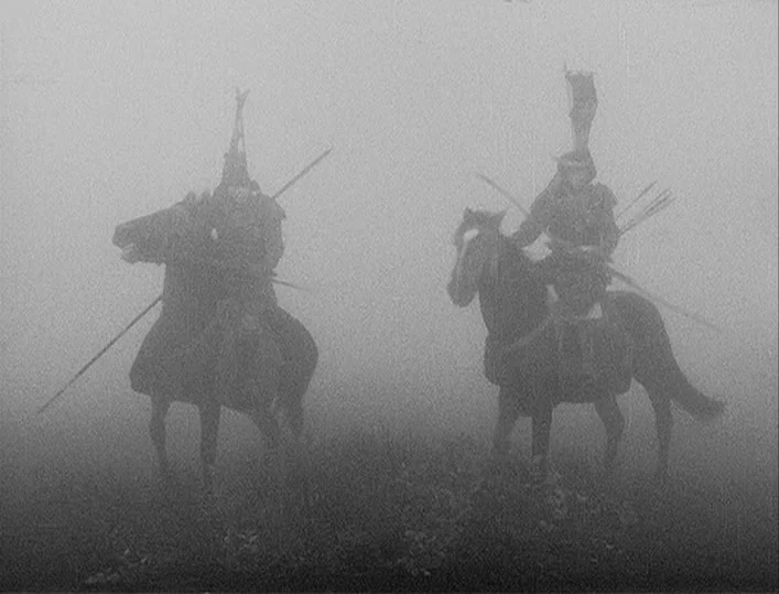 Throne of Blood (1957) movie still: fullbody — Two samurai on horseback stand on a grassy expanse shrouded in dense gray fog. The riders wear…