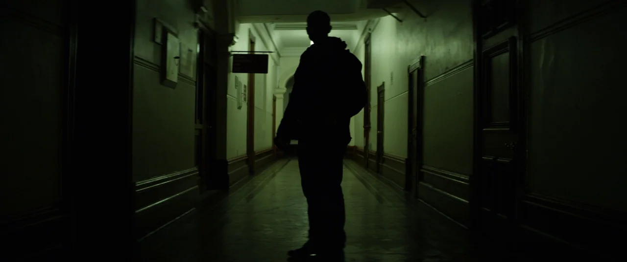 The Empty Man (2020) movie still: fullbody — A long, narrow hospital corridor features high ceilings, panelled walls, and several closed doors. A…