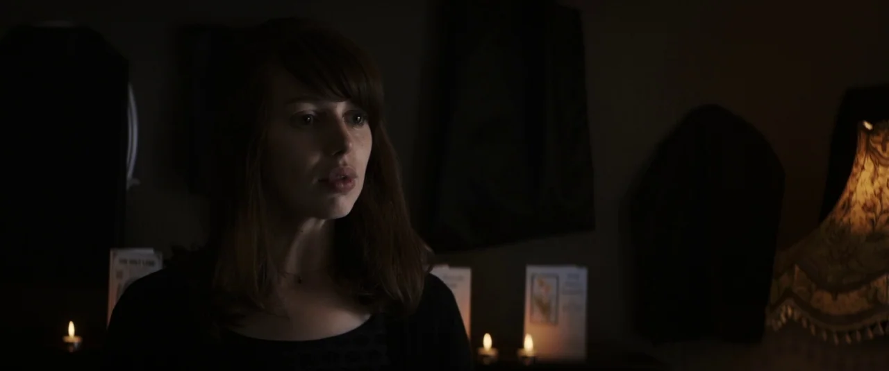 The Hole in the Ground (2019) movie still: medium — A dimly lit room features a woman standing in front of several lit candles. Small greeting cards…