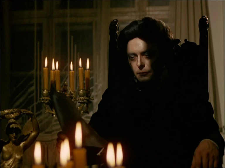 Satan’s Brew (1976) movie still: medium — A dimly lit room contains a person sitting in a dark, ornate high-backed chair. Several burning candles…