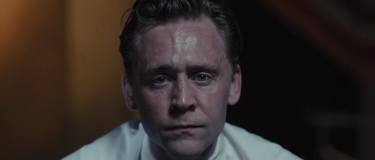 High-Rise (2015) movie still: closeup — A dimly lit, dark space surrounds the figure. A man faces forward, centered in the frame.