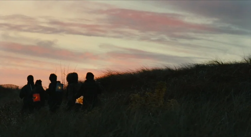 35 Shots of Rum (2008) movie still: wide — A group of people walks across a grassy coastal dune during a twilight sunset. The figures are rendered…