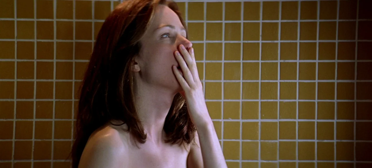 Live Flesh (1997) movie still: closeup — A wall of small golden-brown square tiles creates a textured backdrop. A woman stands in front of the tiles…