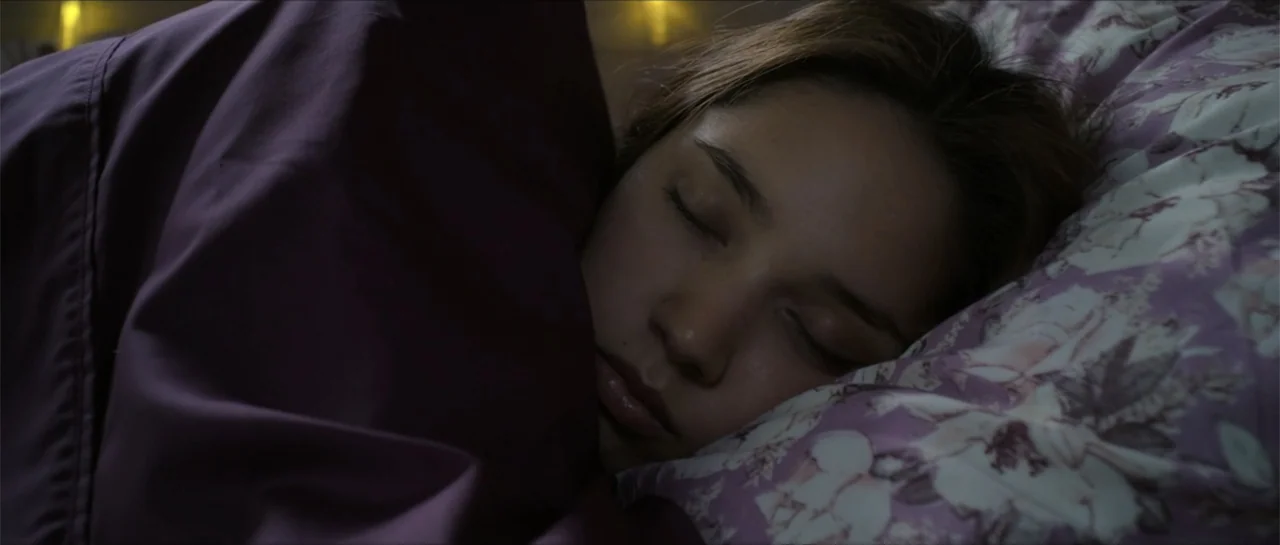 Disconnected 2 (2025) movie still: closeup — A close view shows a person sleeping under a floral patterned blanket. The subject rests their head on…