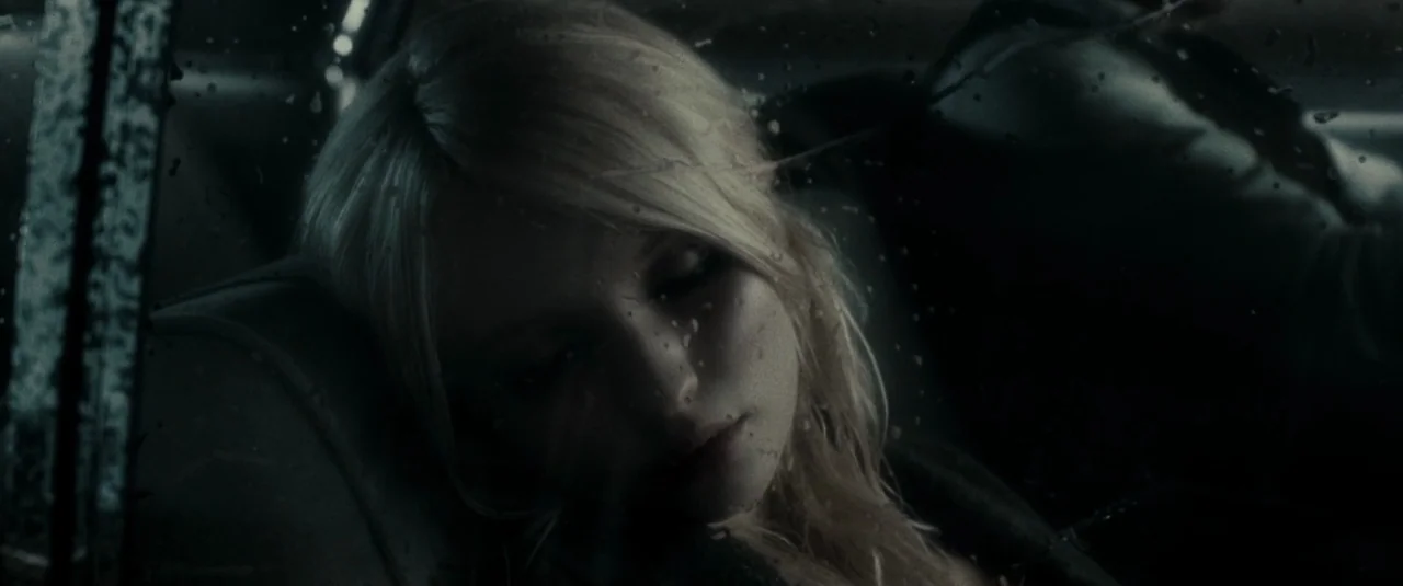 Sucker Punch (2011) movie still: closeup — A dark vehicle interior during a rainy night with blurred street lights outside. A young woman with…