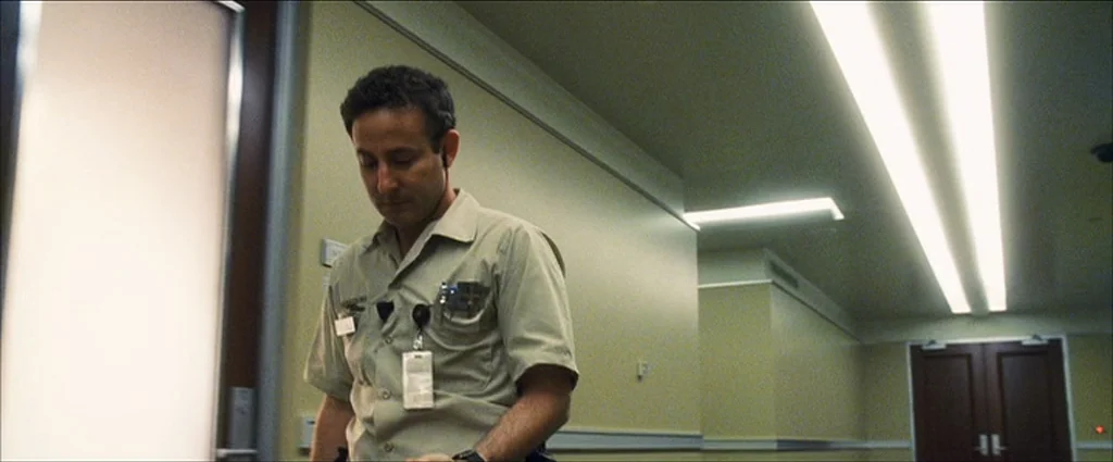 Ocean’s Eleven (2001) movie still: medium — A sterile hallway features pale yellow walls and recessed fluorescent lighting strips. A man in a work…