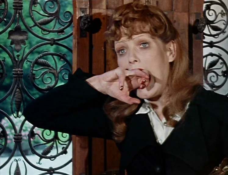 Martha (1974) movie still: closeup — A woman sits before an ornate metal grille near a dark wooden panel. She raises her hand to her open mouth and…