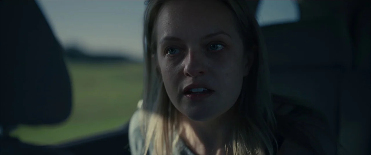 The Invisible Man (2020) (2020) movie still: closeup — A woman sits inside a car during the daytime. She looks forward with her mouth slightly open…
