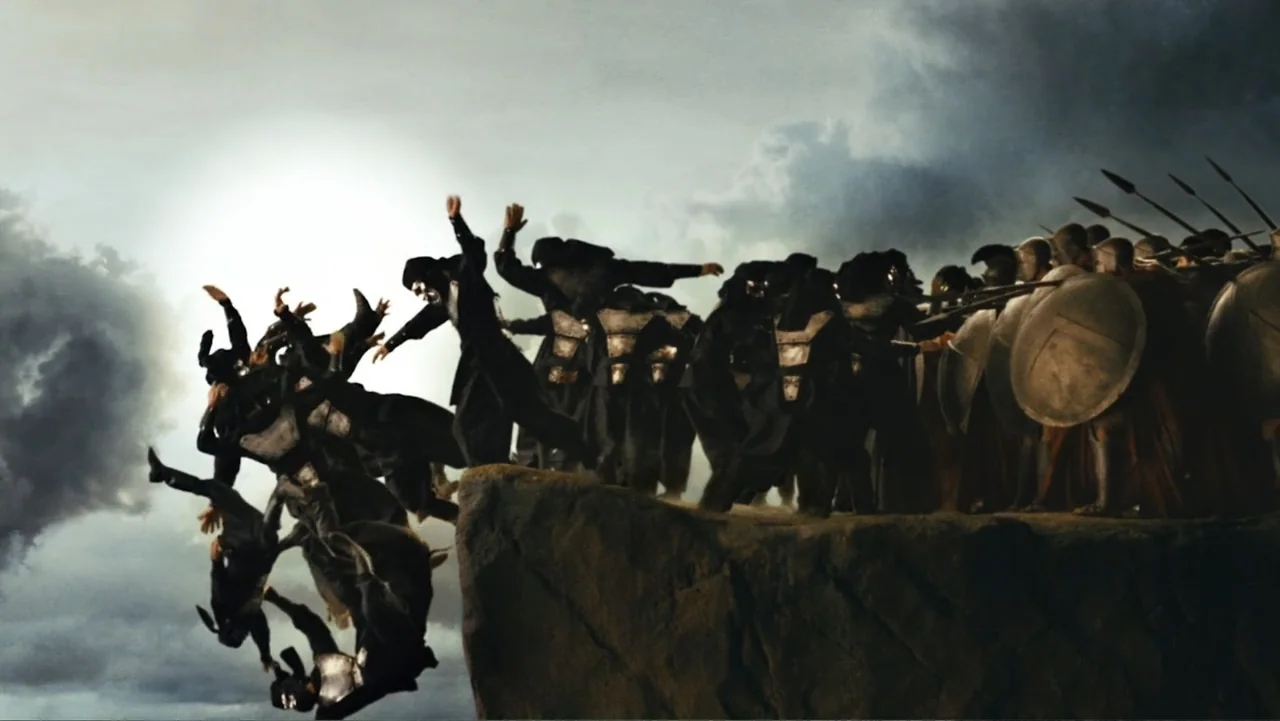 Meet the Spartans (2008) movie still: wide — A jagged rocky precipice stands against a vast, clouded sky at high altitude. Numerous armored warriors…