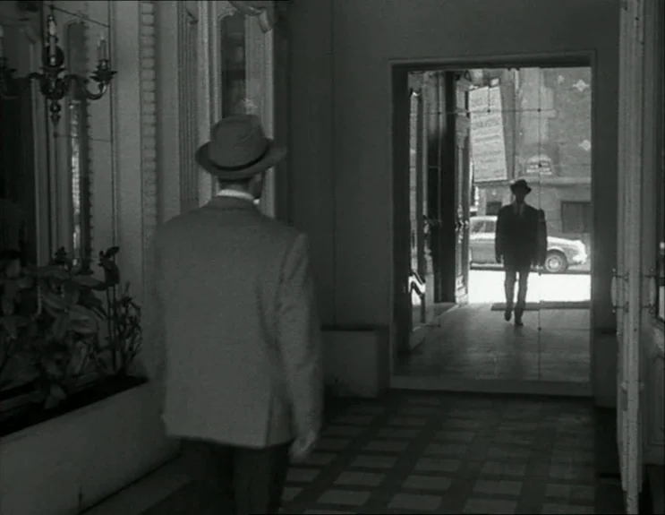 À Bout De Souffle (Breathless) (1960) movie still: medium — An interior lobby features dark tiled flooring and wall-mounted chandeliers flanking the…