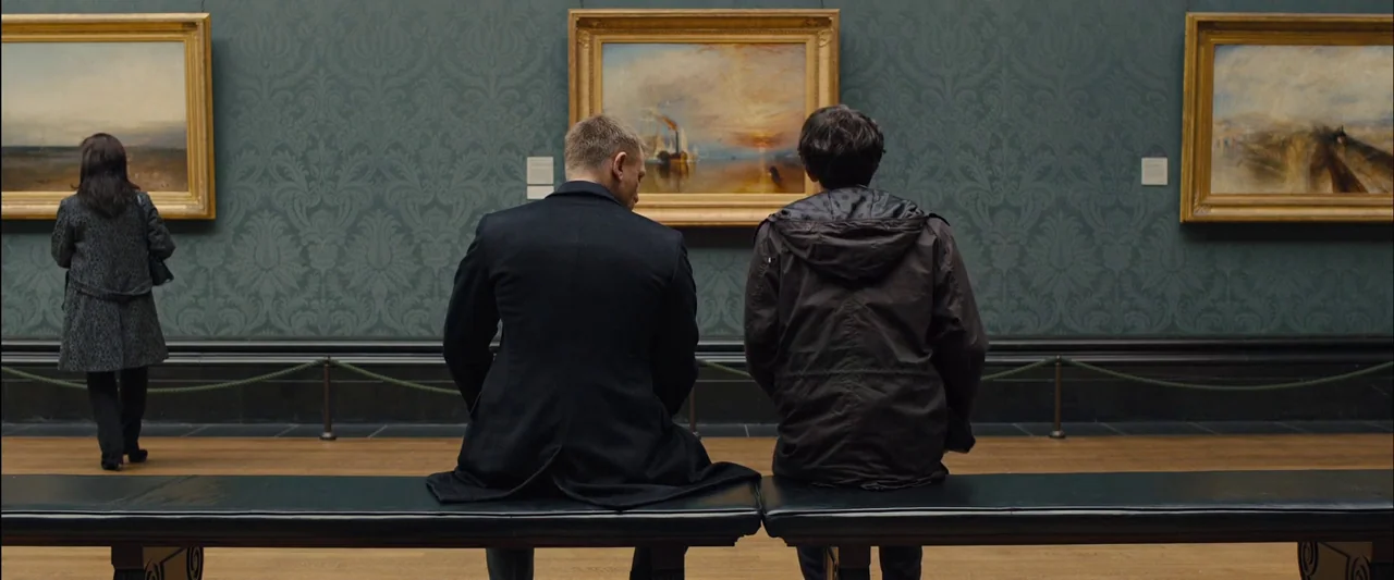 Skyfall (2012) movie still: fullbody — A high-ceilinged museum room displays landscape oil paintings on patterned dark green walls. Two men sit on a…