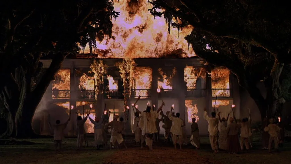 Interview With The Vampire movie still: wide — A large two-story plantation home is fully consumed by bright orange flames at night. A crowd of…