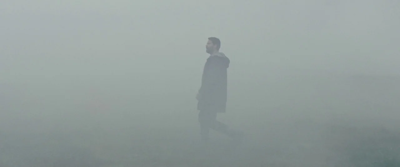 Babel (2006) movie still: wide — An open field is obscured by a dense and uniform layer of heavy fog. A man walks steadily through the featureless…
