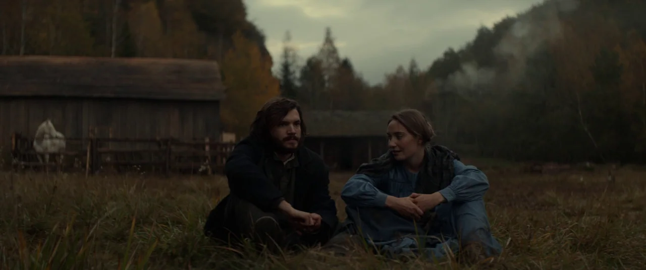 Never Grow Old (2019) movie still: medium — A rural pasture landscape at dusk features a rustic wooden barn and distant trees. A man and woman sit…