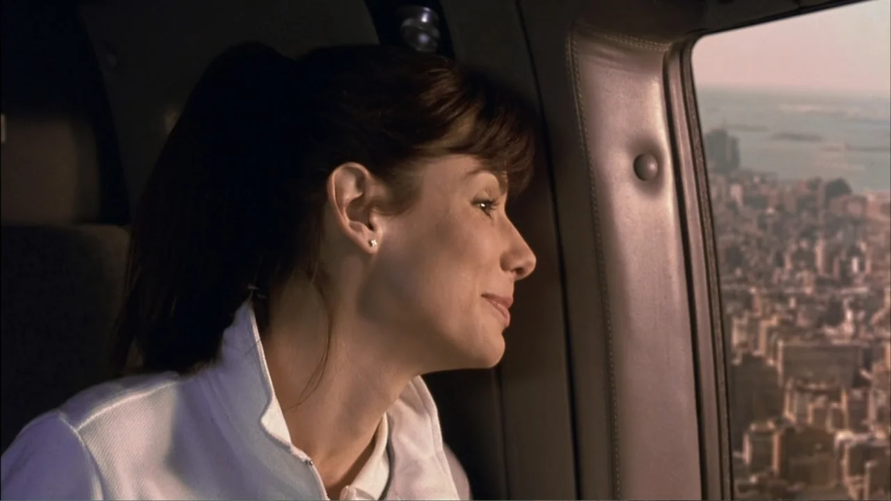 Two Weeks Notice (2002) movie still: closeup — A woman sits inside a helicopter looking out the window at a city. She is positioned against the…