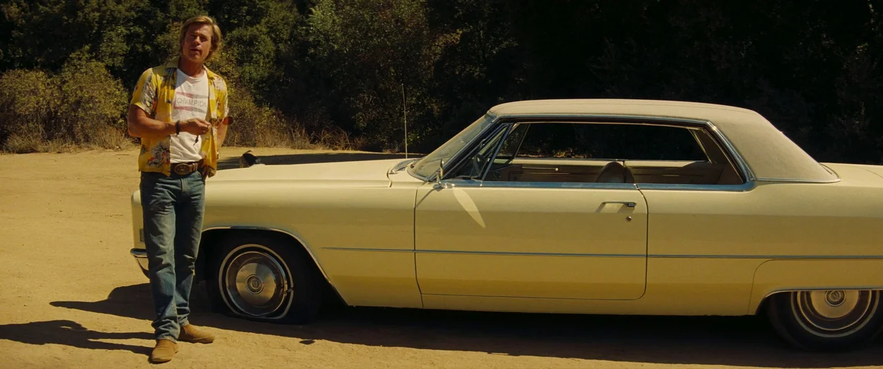 Once Upon a Time… In Hollywood (2019) movie still: fullbody — A dusty dirt lot in a rural setting bordered by dense green trees. A man in a floral…