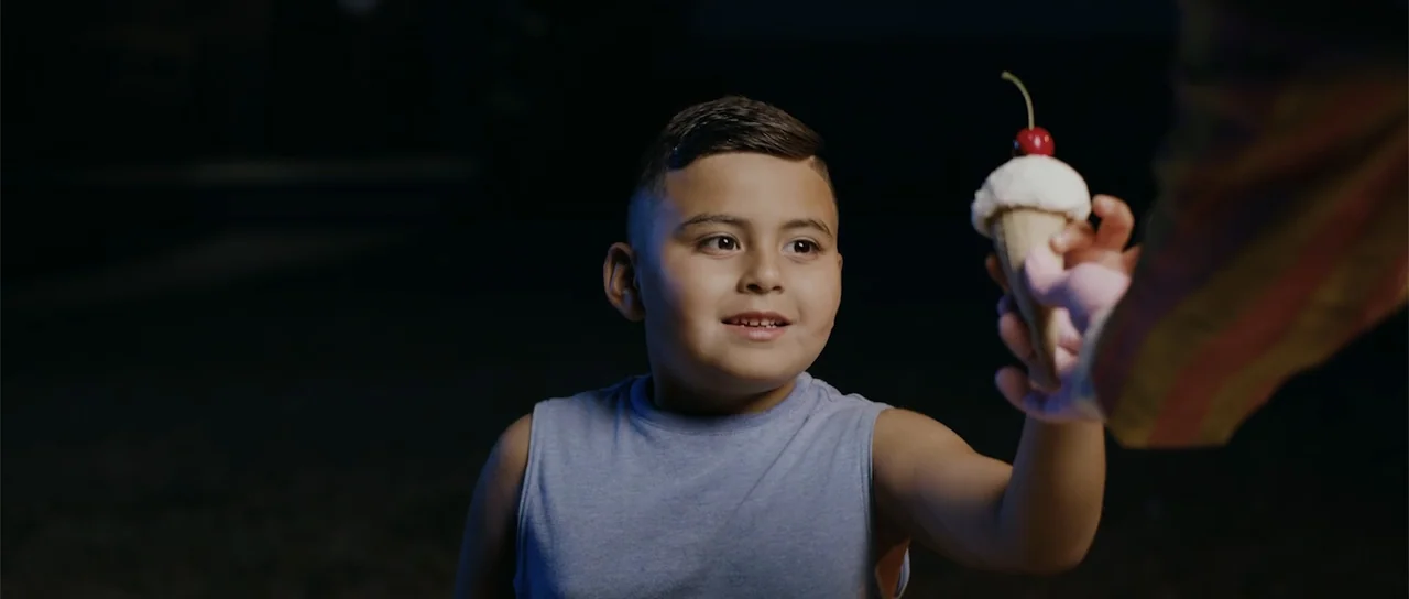 Night of the Missing (2023) movie still: medium — A nighttime outdoor setting with a dark, indistinct background. A young boy looks at an ice cream…