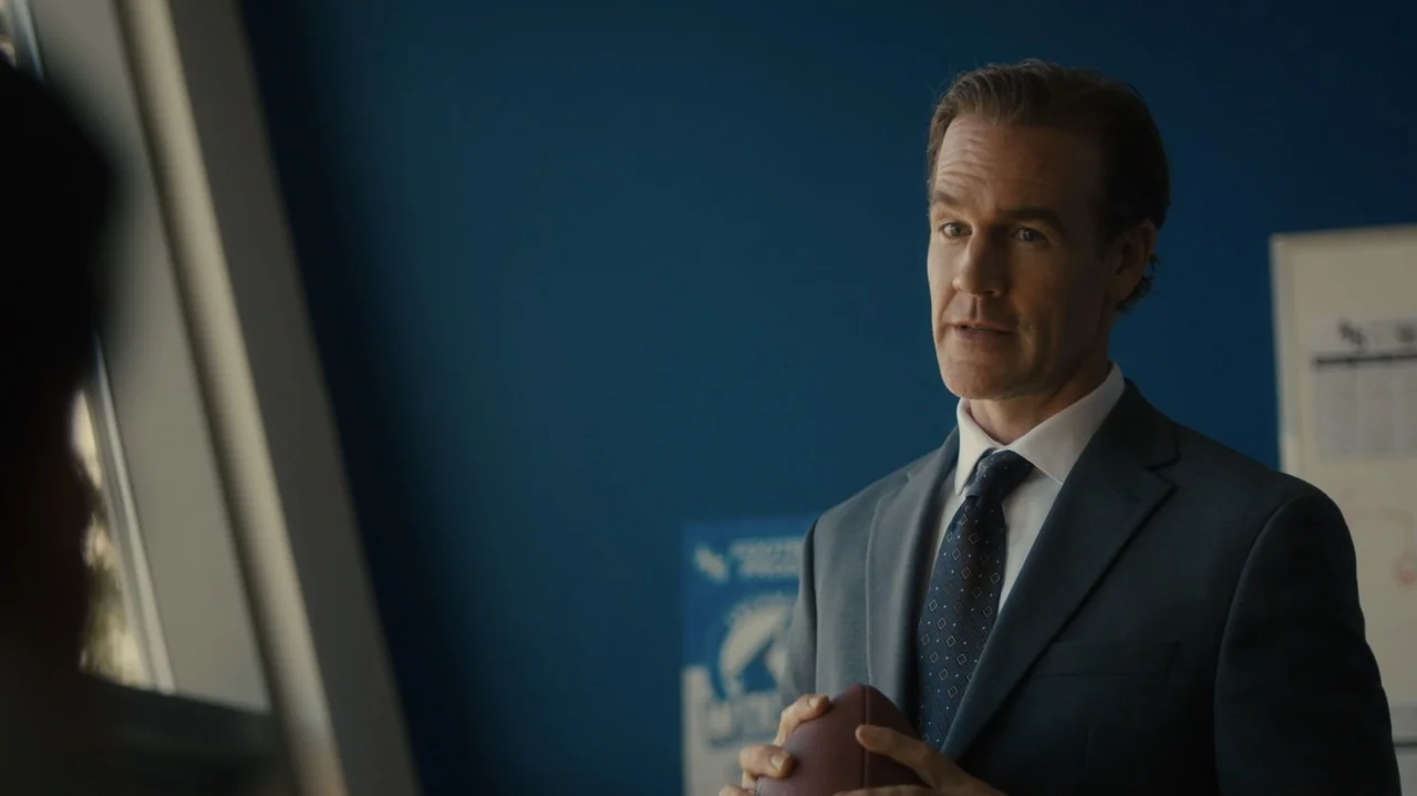 Sidelined: The QB and Me (2025) movie still: medium — A professional office with blue walls and a blurred white board in back. A middle-aged man in…