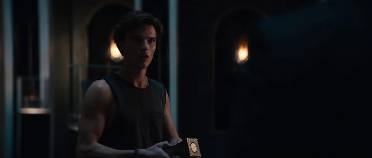 Hellraiser (2022) movie still: medium — A dark, modern museum space features dim warm light glowing from recessed display alcoves. A young man…