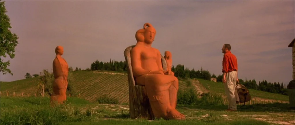 Stealing Beauty (1996) movie still: wide — A rural vineyard landscape with rows of grapevines on a rolling green hillside. A man in a red shirt…