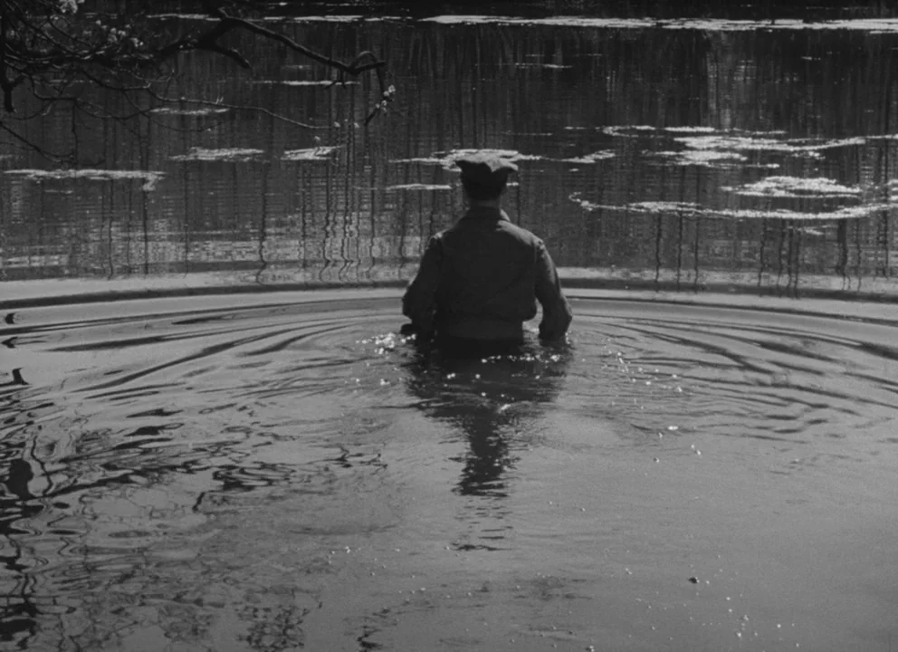 Dead of Night (1945) movie still: medium — A calm, dark pond surface is disturbed by ripples radiating from a lone man. The man in a military jacket…