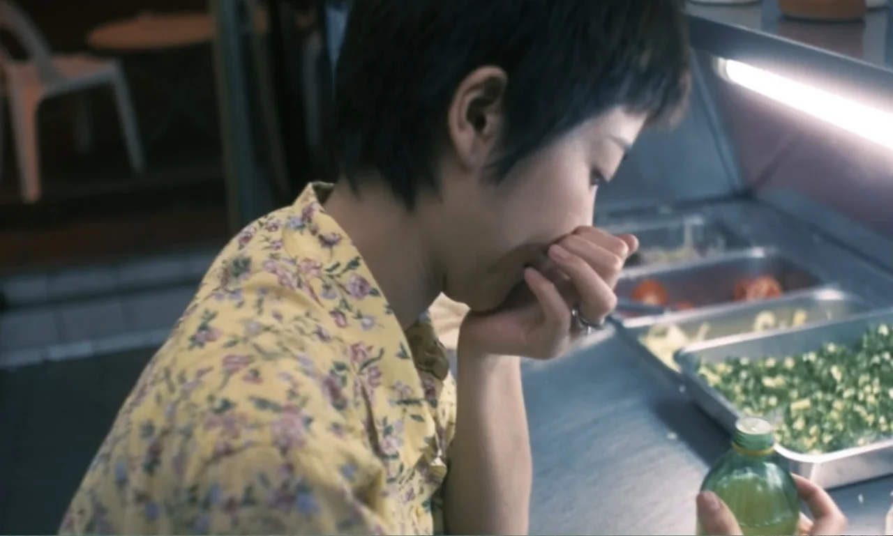 Chungking Express (1994) movie still: medium — A food counter contains metal trays of prepared vegetables under bright overhead light. A woman with…