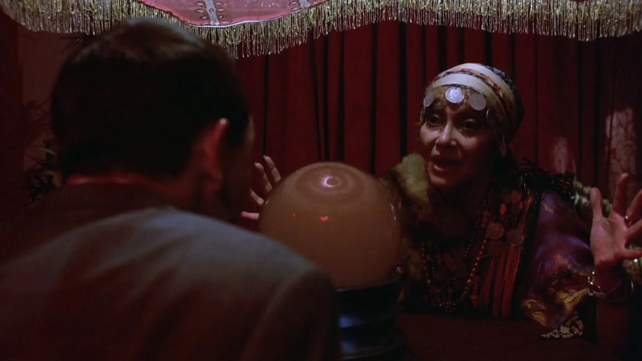 Pee-Wee’s Big Adventure (1985) movie still: medium — A dimly lit fortune teller's tent features red fabric walls and ornate decorative fringe. An…
