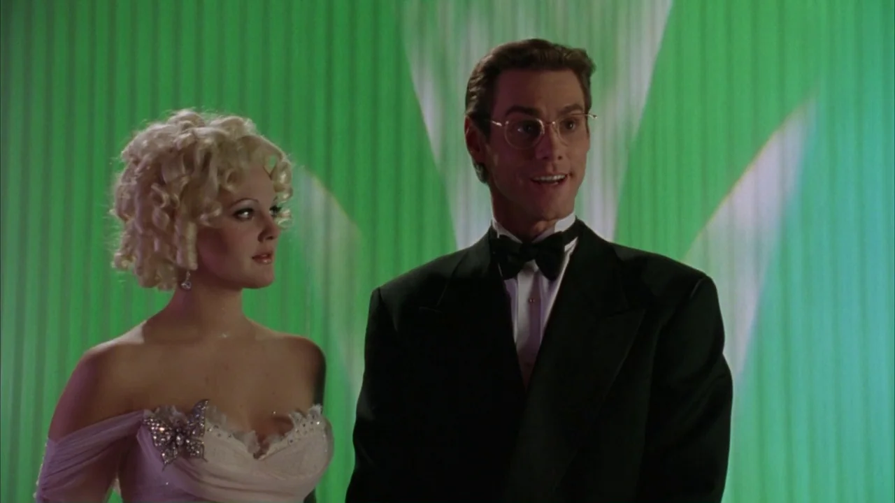 Batman Forever (1995) movie still: medium — A man and woman stand in front of a bright green, ribbed curtain backdrop. The man wears a tuxedo while…