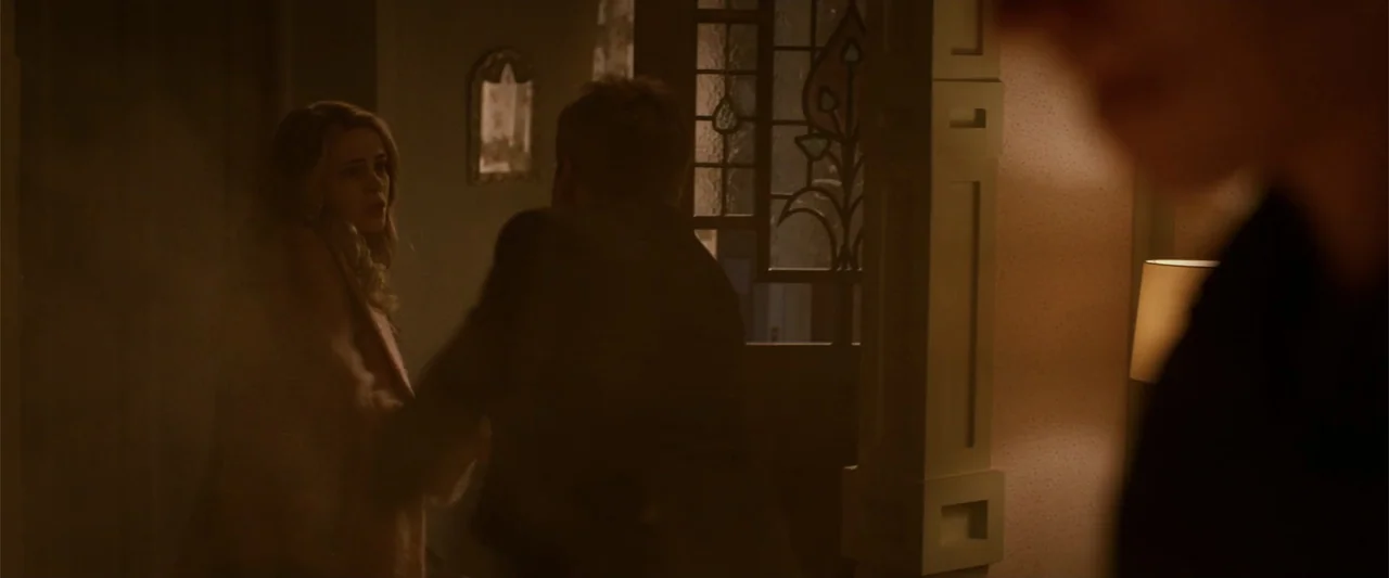 After Ever Happy (2022) movie still: medium — A dimly lit room features a stained glass window pane set into a wooden frame. A man with his back to…