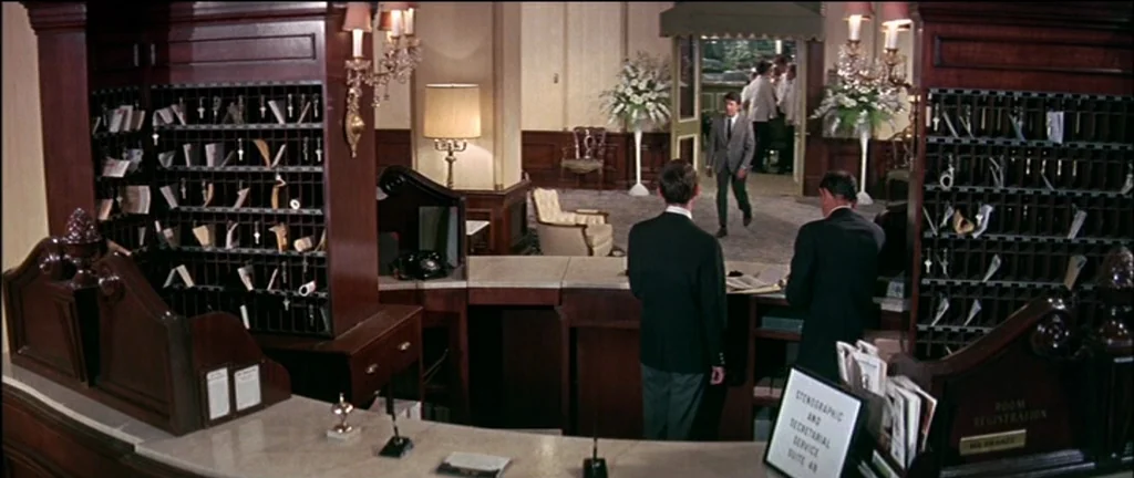 The Graduate (1967) movie still: wide — A spacious wood-paneled hotel registration area features ornate mail slots and elegant lighting fixtures.…