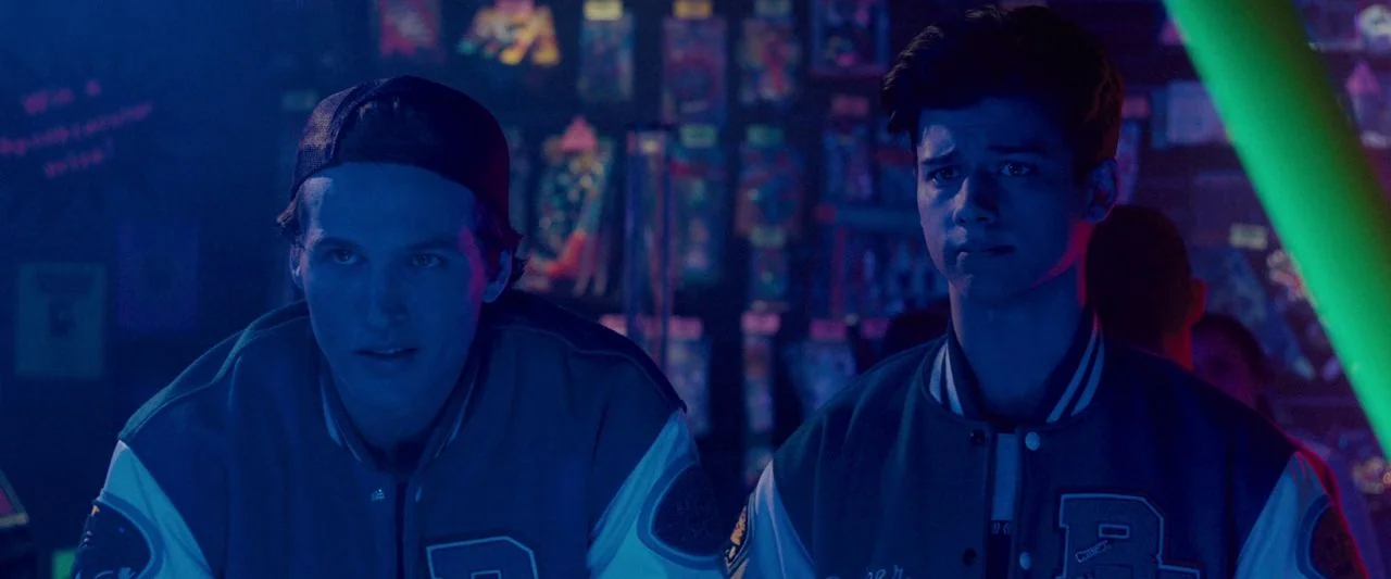 Freaky (2020) movie still: medium — An arcade space with shelves of packaged prizes visible in the blurred background. Two young men in matching…