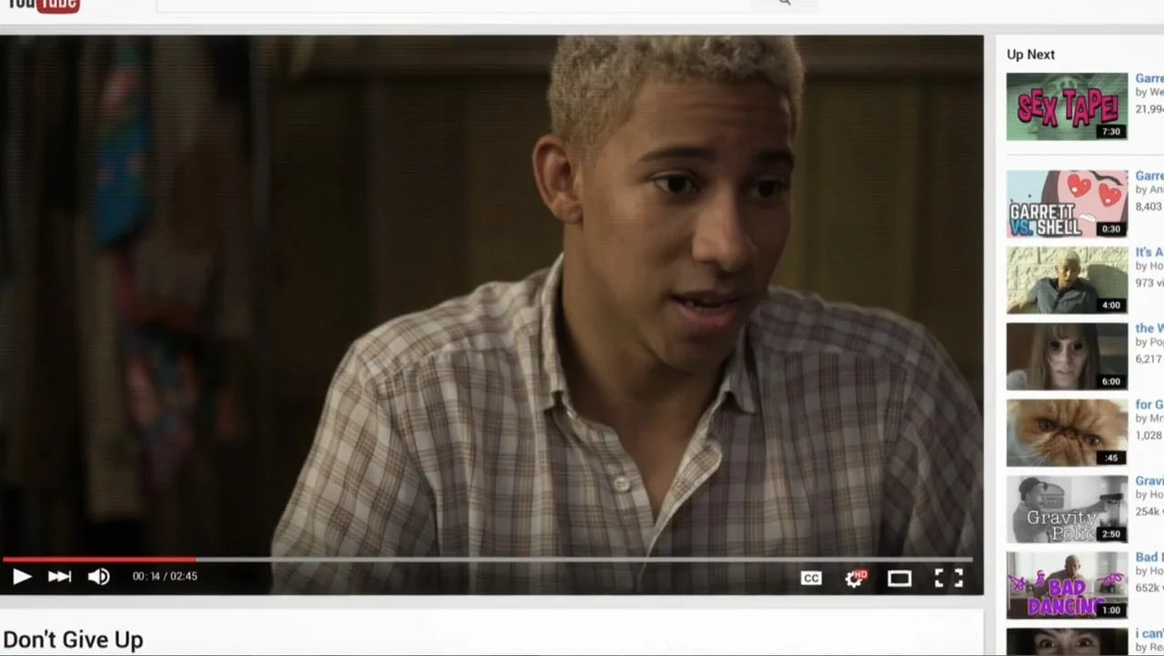 Like.Share.Follow. (2017) movie still: medium — An interior space with wood-paneled walls in the background. A young man with bleached hair speaks…