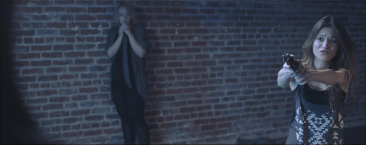 El Último Juego (2025) movie still: medium — An interior space features an exposed red brick wall spanning the background. One woman stands in the…