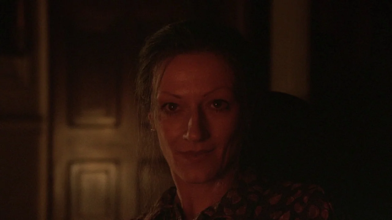 The Lair of the White Worm (1988) movie still: closeup — A woman stands in a dimly lit, dark space with a single warm light. The focus is tightly…