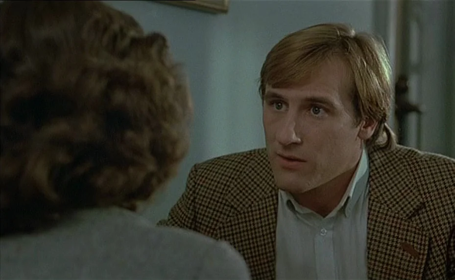 The Woman Next Door (1981) movie still: medium — A man in a houndstooth blazer faces a woman in a dimly lit room. The man maintains eye contact…