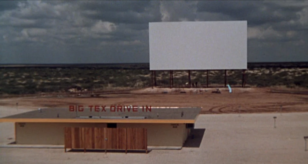 Midnight Cowboy (1969) movie still: establishing — A drive-in theater stands in a wide, arid landscape under a cloudy sky. The Big Tex Drive In…