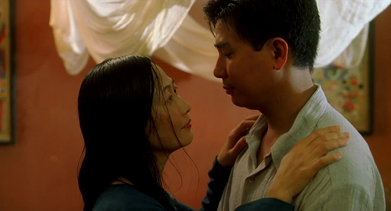 The Vertical Ray of the Sun (2000) movie still: medium — An interior room has light-colored fabric draped in the background against a red wall. A…